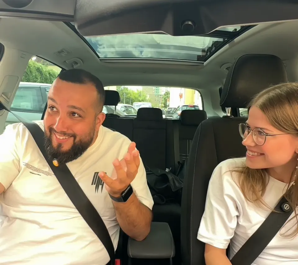 Tolga lacht mit einer Fahrschülerin während der Fahrstunde